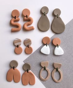 several different shapes and sizes of earrings on a white table with grey paper next to them