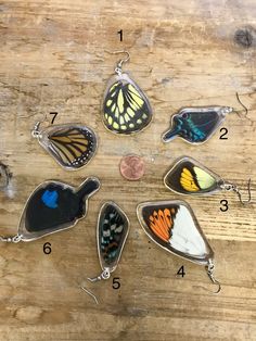 six different butterfly pendants are shown on a wooden surface, with numbers in the middle