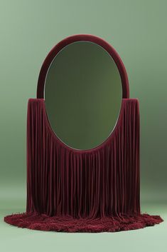 a round mirror sitting on top of a red table next to a circular mirror with fringed edges