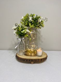 two vases with flowers and candles are on a wooden tray next to a candle