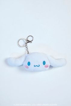 a white stuffed animal keychain with blue eyes and pink cheeks, sitting on a white surface