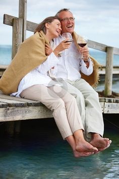 two people sitting on a dock drinking wine