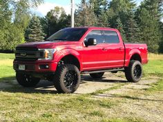 a red truck parked on top of a grass covered field with trees in the background