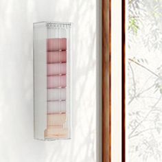 a white wall mounted shelf filled with pink and beige items next to a window in a room