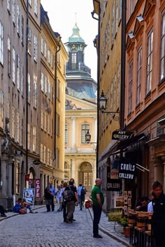 people are walking down an alley way in the old part of town with tall buildings