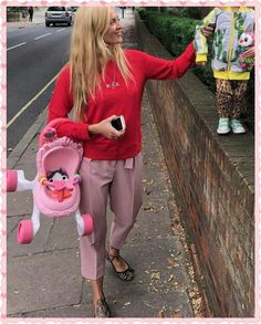 a woman is walking down the sidewalk with her baby in a pink stroller and holding an infant's toy