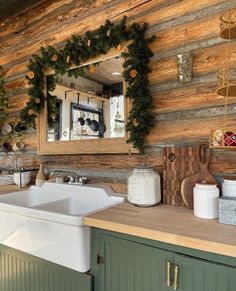 a rustic kitchen decorated for christmas with wreaths and pine cones on the wall above the sink