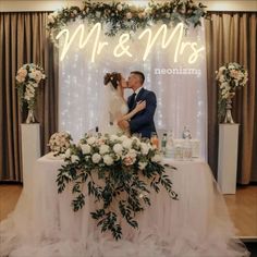 a bride and groom kissing in front of a neon sign at their wedding reception table