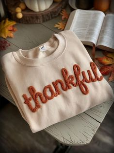 a white sweater with the word thank written on it and an open book in the background