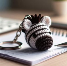 a crocheted zebra keychain sitting on top of a notepad next to a pen