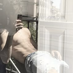 a shirtless man leaning against a window