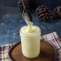 a spoon in a jar filled with liquid on top of a wooden plate next to pine cones