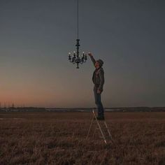 a man standing on a ladder reaching up to a chandelier in the middle of a field