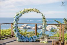 an outdoor wedding setup with blue flowers and greenery on a deck overlooking the ocean