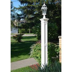 a tall white clock tower sitting in the middle of a lush green park next to a sidewalk