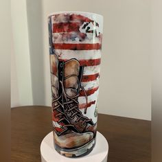 a glass with an american flag and boots on it sitting on a white pedestal in front of a wall