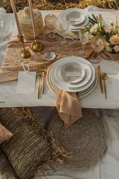 the table is set with white plates and silverware, gold place settings and burlap napkins