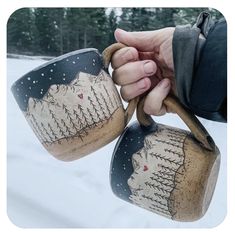 someone holding two mugs in the snow with trees in the backgroung