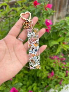 a hand holding a keychain with pictures on it in front of some flowers