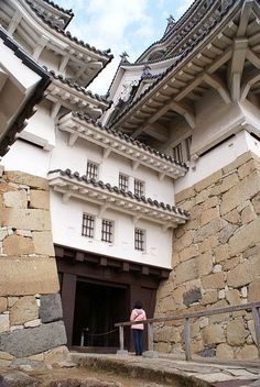 a woman standing in front of a building with stone walls and roofing on it