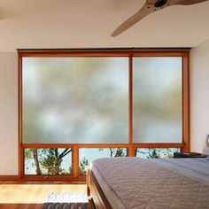 a bedroom with a bed, ceiling fan and large window overlooking the trees in the distance