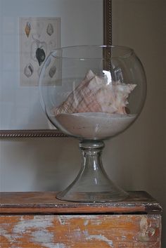 a glass bowl filled with sand and sea shells on top of a wooden table next to a mirror