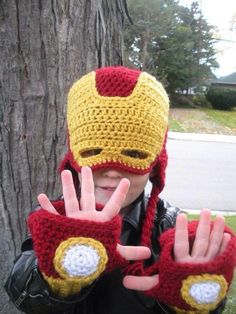 a young boy wearing a knitted iron man hat and mittens making the peace sign