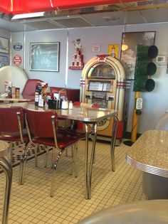 a diner with red chairs and tables in the middle of the room, next to an old juke oven