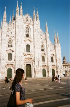 a woman is standing in front of a large building with many spires and windows