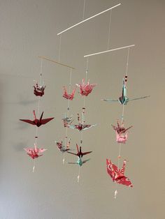 a group of origami birds hanging from strings on a wall next to a white wall