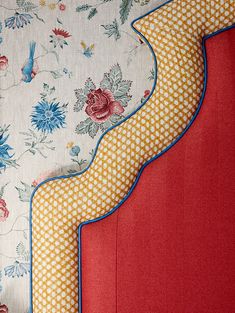 an upholstered headboard with blue and red flowers on white fabric, against a wallpapered background