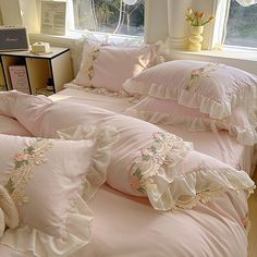 a bed with pink comforters and pillows on top of it next to a window