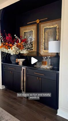 a living room with black cabinets and flowers in vases on the counter, and an open door leading to another room