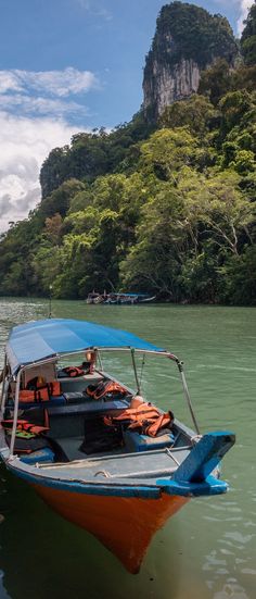 a blue and orange boat floating on top of a river next to a lush green hillside