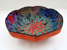 an orange bowl with blue and red flowers painted on the inside is sitting on a white surface