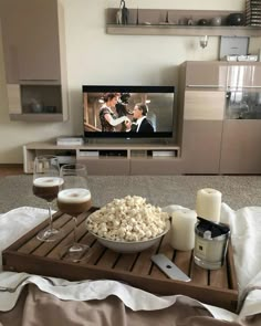 a tray with popcorn and wine on it in front of a flat screen tv