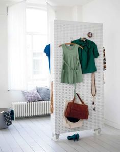 a coat rack with clothes and purses hanging from it's sides in a white room