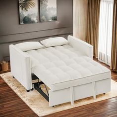 a white couch sitting on top of a wooden floor next to a window with curtains