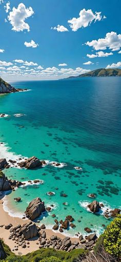 an aerial view of the beach and ocean with rocks in the foreground, blue water and white clouds overhead