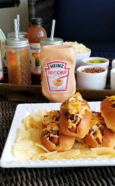 two hot dogs with toppings sit on a plate next to chips and condiments