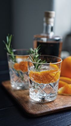 two glasses with orange slices and rosemary garnish sit on a wooden cutting board