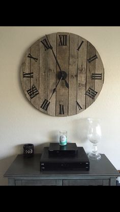 a large clock mounted to the side of a wall above a table with a remote control