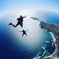 two people are jumping in the air over an island and ocean with blue water below