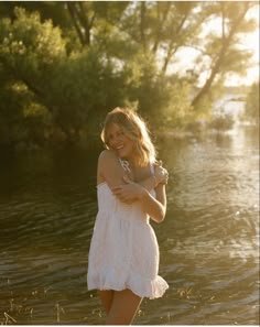 a woman in a white dress standing by the water with her arms around her neck