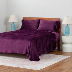 a bed with purple sheets and pillows on top of it in a bedroom next to two lamps