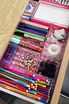 an open drawer with many different types of pens and pencils in it on top of a wooden table