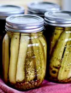 four jars filled with pickles sitting on top of a pink towel