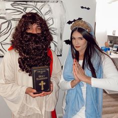 two people dressed up as jesus and mary holding a book in front of their faces