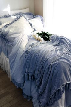 an unmade bed with blue ruffled sheets and pillows on it, in front of a window