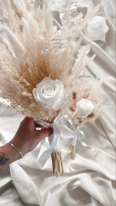 a person holding a bouquet of flowers on top of a white bed sheet covered in sheets